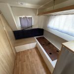 Photo de la cabine tribord du bateau avec un sommier pour un lit simple et un meuble de rangement en bois situé devant lui.