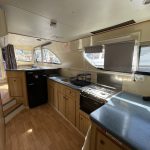 Photo de la cuisine du bateau avec des murs de couleur beige et le même parquet en bois clair que dans le salon. La cuisine est équipée d'un réfrigérateur noir, d'un évier et d'un four.