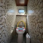 Image des toilettes du bateau avec la lunette des toilettes avec un motif représentant une bouée de sauvetage. Les murs sont en mosaïques beige, marron et noir.