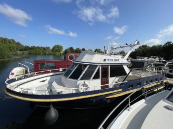 Vue d'ensemble du bateau WHY NOT. Sa coque est bleu foncé avec une bande jaune au-dessus.