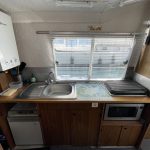Photo de la cuisine du bateau avec des meubles en bois. On y voit un évier à gauche, un frigo en bas à gauche et un micro-ondes en bas à droite.