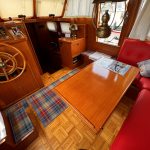 Photo montrant le poste de pilotage en bois du bateau à gauche. A droite, le canapé avec la table carré.