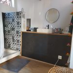 Photo de la salle de bain de la chambre parentale. Elle est composée d'une douche avec une mosaïque noire et blanche ainsi qu'un grand meuble où est situé un évier.