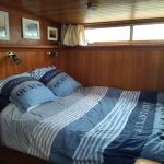 Photo de la première cabine du bateau. Elle est équipée d'un lit double. On voit sur la photo le lit double avec une parure de lit aux couleurs bleues.