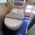 Photo de la cabine arrière du bateau avec les murs en bois beige clair et une moquette bleu foncé. Au centre, un lit double avec le bout arrondi.