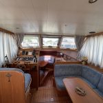 Photo de la pièce à vivre du bateau. On voit à droite le poste de pilotage intérieur en bois, au fond la cuisine et à gauche une banquette bleu.