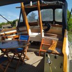 Photo de la terrasse du bateau tout en bois. On y trouve le poste de pilotage extérieur ainsi qu'une table de jardin en bois.