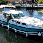 Nicols 1100 river cruiser Lodève (1998) – front three-quarter view, two people at the helm